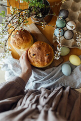 Homemade easter bread in hands on background of natural dyed eggs and spring blossom on rustic table in room. Happy Easter! Woman holding freshly baked easter cake. top view