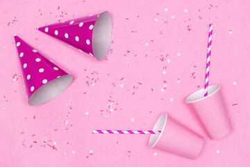 Paper cups, striped drinking straws, party hats with candy sprinkles on pink background. Birthday party concept. Copy space
