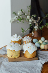 Happy Easter!  Homemade easter bread, natural dyed eggs and spring blossom on rustic table in room. Stylish freshly baked easter cake with sugar glaze and sprinkles, traditional ukrainian bun