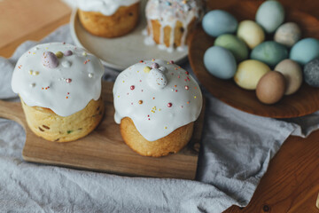 Homemade easter breads, natural dyed eggs and spring blossom on rustic table in room. Happy Easter! Stylish freshly baked easter cake with sugar glaze and sprinkles, traditional ukrainian bun