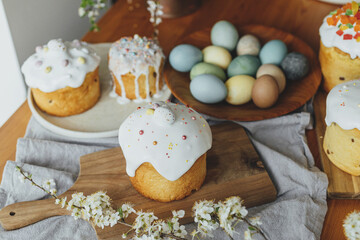 Fototapeta na wymiar Homemade easter breads, natural dyed eggs and spring blossom on rustic table in room. Happy Easter! Stylish freshly baked easter cake with sugar glaze and sprinkles, traditional ukrainian bun