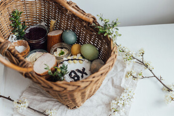 Natural dyed easter eggs, easter bread, ham, beets, butter, cheese in wicker basket decorated with...