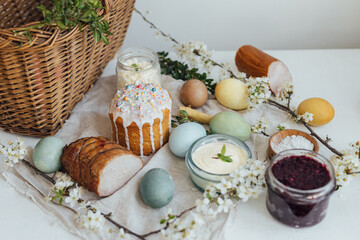 Traditional Easter basket food. Natural dyed easter eggs, stylish easter bread, ham, beets, butter, cheese on rustic wooden table with spring blossoms and linen napkin. Happy Easter!
