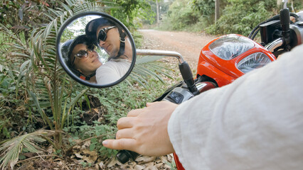 Love couple on red motorbike in white clothes to go on forest road trail trip. View in the rear-view mirror. Two caucasian tourist woman man drive on scooter. Motorcycle rent, safety helmet.