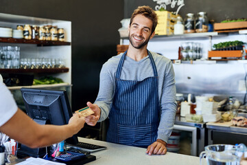 Hes got smiles for every single customer. Shot of a handsome young businessman taking payment from a customer.