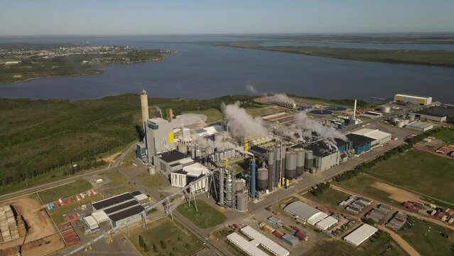 Aerial view of paper mill factory with smoky chimneys in front to River in Fray Bentos,Uruguay - Environmental pollution of earth