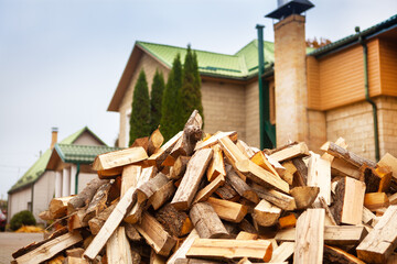 A pile of split firewood for heating the house, unloaded in the yard, against the backdrop of the house, natural heating sources.