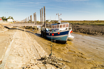 Bateau de pêche artisanale amarré à un ponton en bois dans un chenal à marée basse, posé sur...