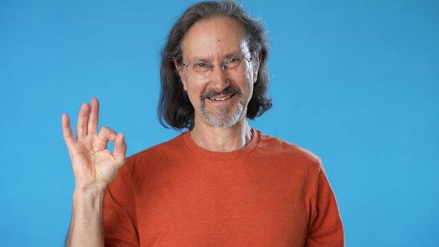 Smiling mature gray-haired mustache bearded man 50s 60s years old showing okay ok zero fingers gesture isolated on solid blue background studio portrait