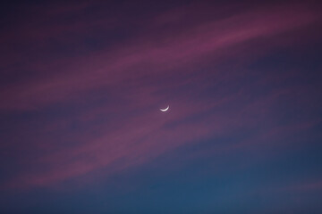 Luna creciente entre nubes y cielo narajan durante un atardecer espectacular.