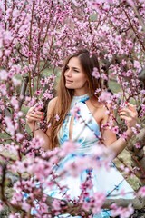 Young beautiful woman in golzbe dress and long hair is enjoying with blossoming peach trees