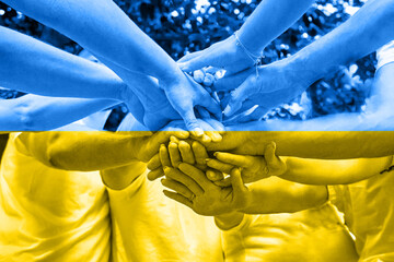 A diverse group of people stacking hands. Concept of Ukrainian patriotism on yellow-blue flag background. War Russia against Ukraine