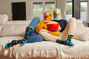 A couple with bird masks watching a movie on the sofa