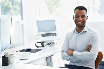 Young, modern and trendy - Todays businessman. A handsome young african american businessman sitting at his desk with his arms folded.