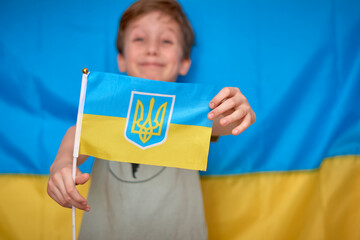 Boy holding in hands Ukrainian flag on yellow-blue background. War of Russia against Ukraine