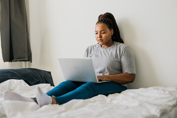 African american young woman using laptop on bed - technologies and communication and social network concept