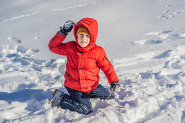 Fototapeta na wymiar Funny little boy in blue winter clothes walks during a snowfall. Outdoors winter activities for kids. Cute child wearing a warm hat low over his eyes catching snowflakes with his tongue