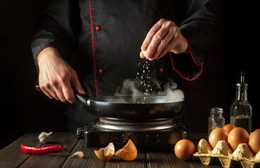 The chef adds salt while cooking eggs in pan. Work environment on kitchen table. Menu idea for a...