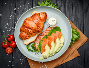 Sandwich. Croissant with salmon, cream cheese, avocado and vegetables.