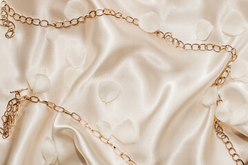 Golden chain and white petals on a silk beige background, space for text.