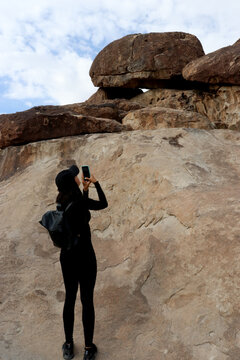 woman taking photos of rocks with self phone in the desert 