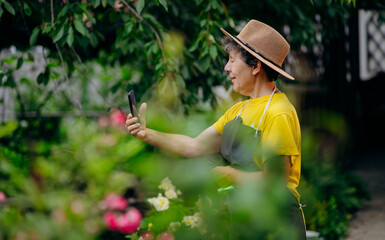 Senior woman gardener in a hat working in her yard and speaks on the phone. The concept of gardening, growing and caring for flowers and plants.