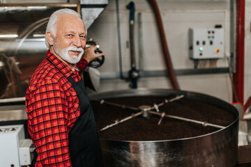 Senior man operating coffee roasting machine in coffee shop. Coffee industry.