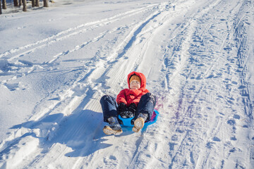 happy and positive little boy enjoying sledding and cold weather outdoor, winter fun activity concept