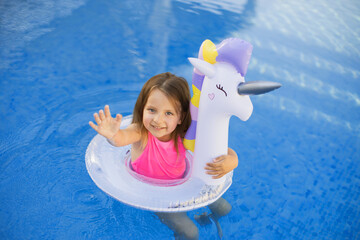 Little girl in swimming pool with inflatable toy ring unicorn. Kids swim on summer vacation....
