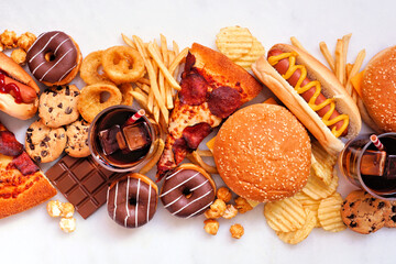 Junk food table scene scattered over a white marble background. Collection of take out and fast...