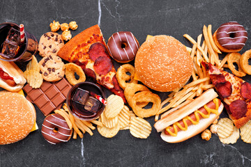 Junk food table scene scattered over a dark background. Mixture of take out and fast foods. Pizza,...