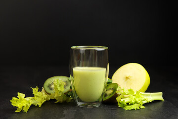 Green smoothie in a glass cup on a black background. Celery, apples, kiwi and mint. Superfoods, detox, diet, healthy food.