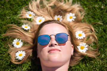 The portrait of beautiful woman in sunglasses lying in the field with chamomile flowers in hair.