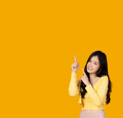 Smiling asian young woman pointing hand to empty space and looking at camera stand over colorful yellow background with happiness and smile face imaginary on top of finger for insert advertisement