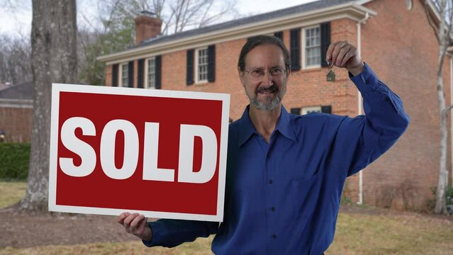 Smiling real estate agent holding SOLD sign and holding icon house key ring in front of a house.