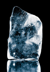 Crystal clear natural ice block on a black reflective surface. Ice piece.