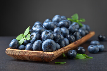Fototapeta premium Blueberries with green leaves in old wooden dish.