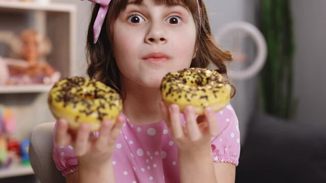 Caucasian child girl with eating disorder eating two donuts quickly and at the same time. School girl is eating two donuts at the same time. Sweet addiction and binge eating concept