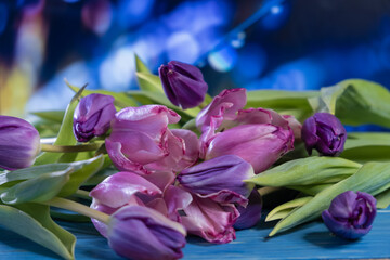 The flowers are pink with green leaves on a blue wooden table. Tulips