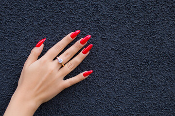 Girl's hand with red manicure and ring on dark background