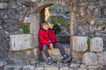 Fototapeta premium Young tourist boy enjoying a view of Kotor Bay, Montenegro. Kotor Old Town Ladder of Kotor Fortress Hiking Trail. Aerial drone view