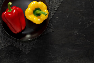 Sweet Bulgarian peppers, two - red and yellow, on a black plate on dark background, top view, space to copy text.