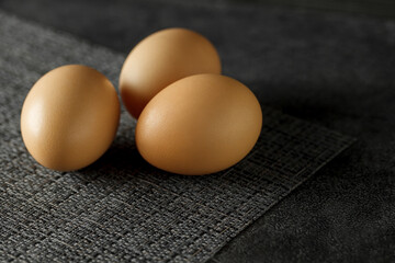 Three whole chicken eggs on dark surface, selective focus.
