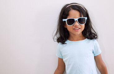 Mom says Im the coolest kid on the block. Shot of an adorable little girl wearing sunglasses while standing against a wall.