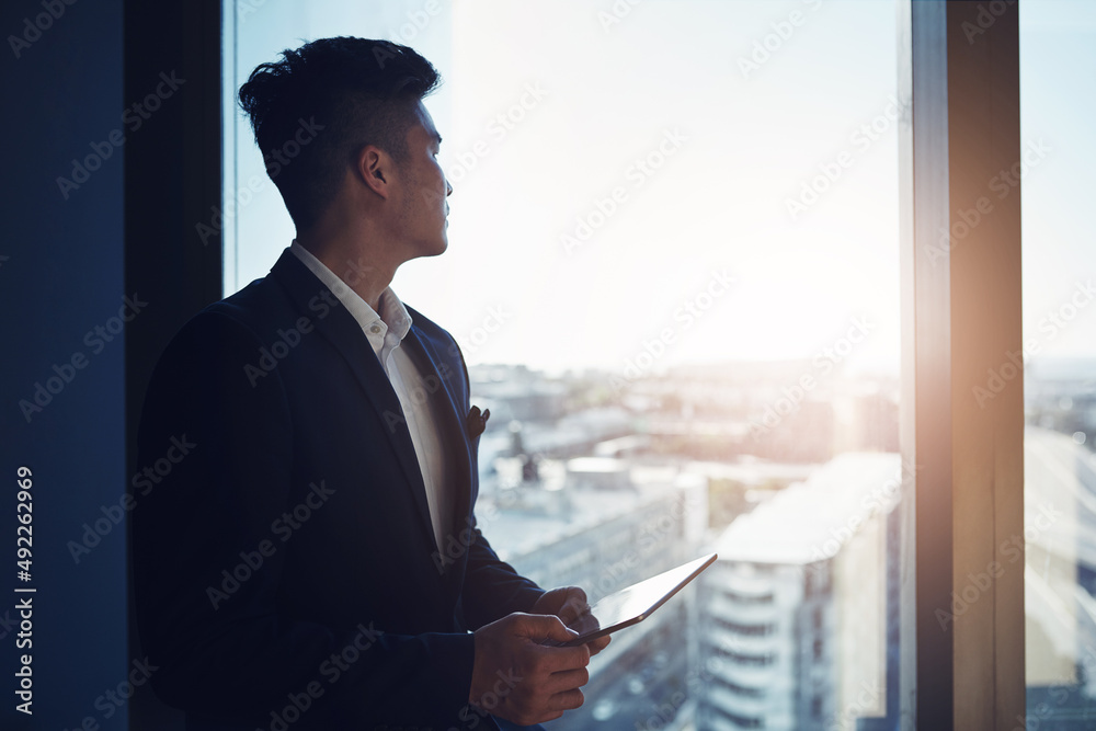 Poster look to the future of business. shot of a young businessman using a digital tablet while looking out