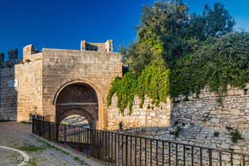 The village of Tarquinia, Viterbo, Lazio, Italy - The access arch through the ancient defensive walls of the city, with the lookout tower. The cobblestone street. The brick and stone wall.