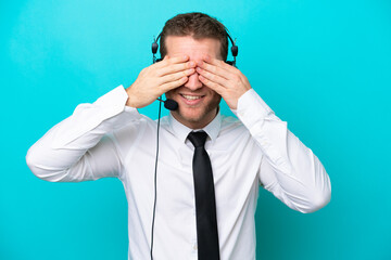 Telemarketer caucasian man working with a headset isolated on blue background covering eyes by hands