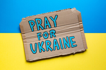 Hand drawn sign with Pray For Ukraine slogan on Ukrainian flag.
