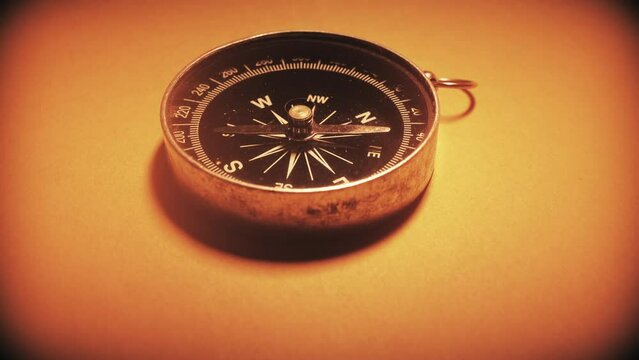 Macro close-up shot of antique compass rotating on old parchment paper texture. Shot on 4K DSLR..