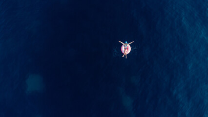 Aerial view of young brunette woman swimming on the inflatable big donut in the blue sea. Top view of slim lady relaxing on her holidays Adriatic sea.